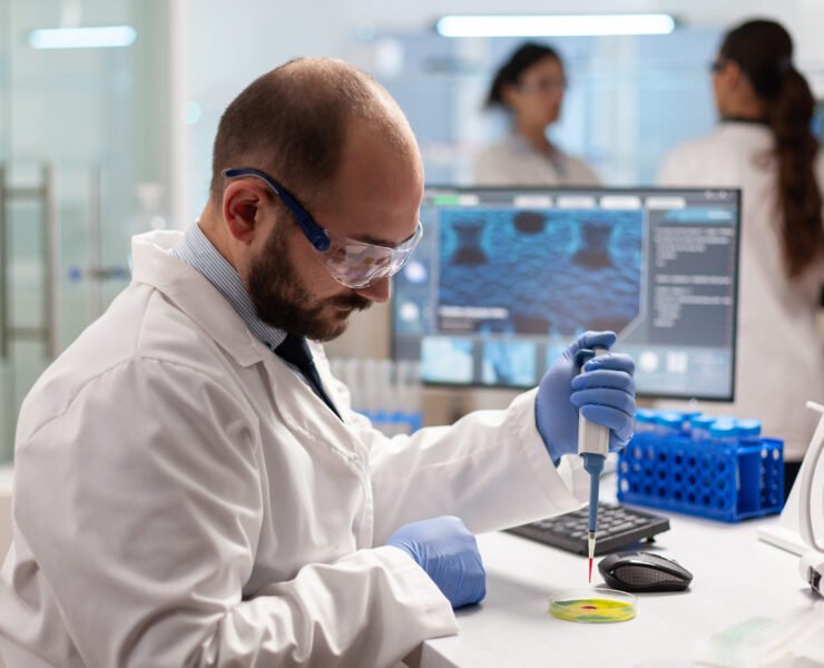Biochemistry health care scientist testing blood sample using micropipette on petri dish. Team of researchers examining virus evolution using high tech for vaccine development.