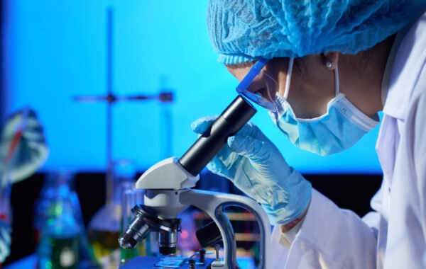 Profile view of concentrated Asian microbiologist examining sample with help of modern microscope while wrapped up in work at dim laboratory