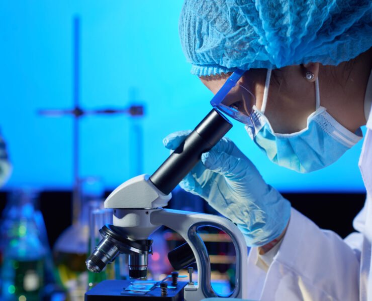 Profile view of concentrated Asian microbiologist examining sample with help of modern microscope while wrapped up in work at dim laboratory